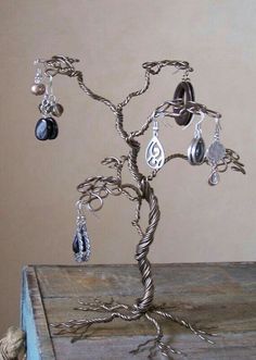 a wire tree with earrings on it sitting on top of a wooden table next to a wall