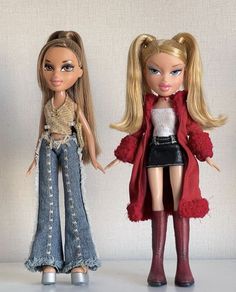 two dolls standing next to each other in front of a white wall and wearing jeans