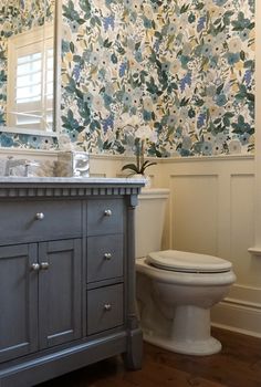 a white toilet sitting next to a sink in a bathroom under a large floral wall paper