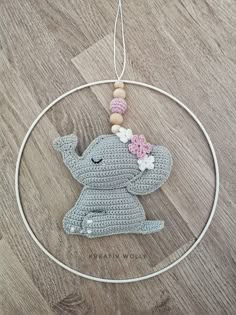 a crocheted elephant ornament hanging from a hoop on a wooden floor