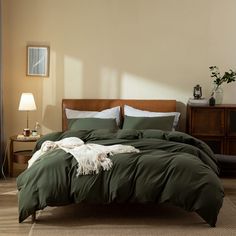 a bed with green sheets and pillows in a room next to a lamp on a table