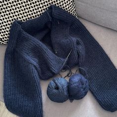 a blue knitted scarf and ball of yarn sitting on a couch next to a pillow