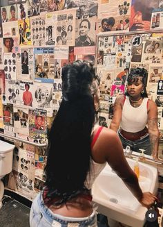 a woman standing in front of a bathroom sink next to a wall covered with posters