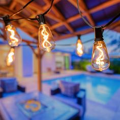 an outdoor dining area with lights hanging from the ceiling and pool in the back ground