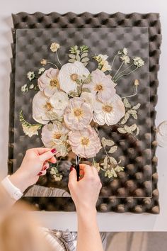 a woman is working on a flower arrangement in front of a black background with white and pink flowers