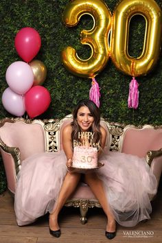 a woman sitting on a couch with a cake in front of her and balloons behind her