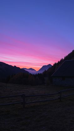 the sun is setting in the mountains behind a wooden fence with a barn on it