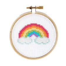 a cross stitch rainbow on a white background with a wooden hoop hanging from it's side