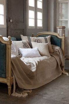 a bed with many pillows on top of it and two windows in the back ground