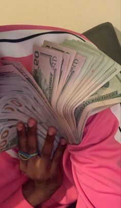 a woman is hiding her face behind stacks of money in a pink shirt and green head scarf