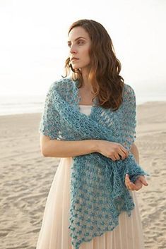 a woman standing on top of a beach wearing a blue crocheted shawl