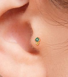 a close up of a person's ear with a small green and yellow diamond on it