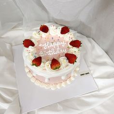 a birthday cake with white frosting and strawberries on top is sitting on a sheet