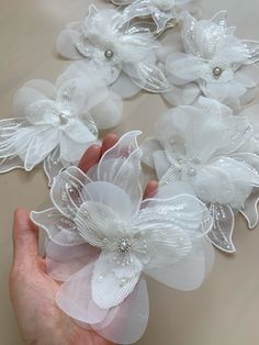 a hand holding some white flowers on top of a table