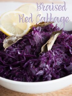 a white bowl filled with red cabbage and lemon wedges on top of a wooden table