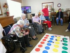 elderly people sitting in wheelchairs playing a board game with colorful circles on the floor