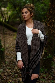 a woman standing in the woods wearing a brown and black knitted ponchy