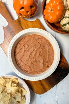 a white bowl filled with red dip surrounded by pumpkins and corn chips on a wooden cutting board