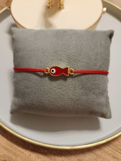 a red cord bracelet sitting on top of a white plate next to a small pillow