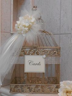 a birdcage with a name tag and flowers on the top is sitting next to a white rose