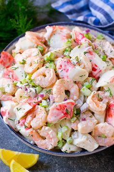 a bowl filled with shrimp salad next to lemon wedges