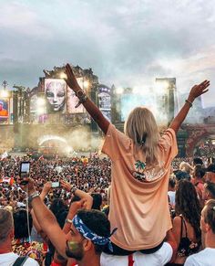 a woman standing in front of a crowd at a music festival with her arms up