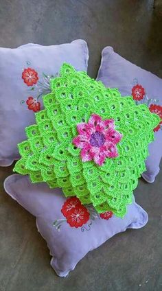 two crocheted pillows on top of each other with pink and green flowers in the middle