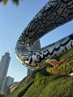 an art piece in the shape of a snake on top of a hill with tall buildings in the background