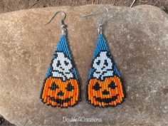 a pair of beaded earrings with pumpkins on them sitting on top of a rock