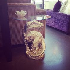 a glass table with an animal statue on it in front of a couch and chair