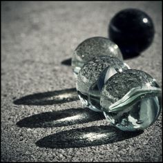 three glass balls sitting on the ground next to each other, with one black ball in the background