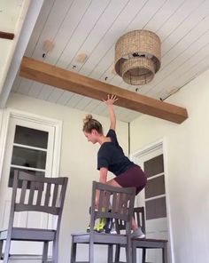 a woman standing on top of a wooden chair in front of a light fixture above her head