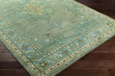 a green rug with an ornate design on the top and bottom, sitting on a wooden floor