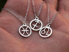 two silver necklaces with symbols on them are held in the palm of someone's hand