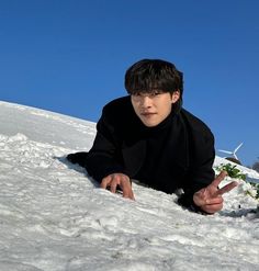 a young man laying in the snow with his fingers up