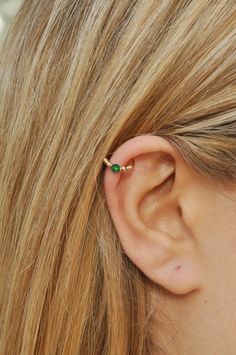 a close up of a person wearing a gold ear cuff with a green bead