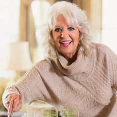 an older woman sitting at a table with two glasses in front of her and smiling