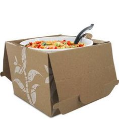 a cardboard box filled with food on top of a white table next to a spoon