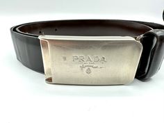 Prada skinny leather belt with logo silver tone clamp buckle. Size: 70 cm/28" Label: Prada, Made in Italy Condition: Fair condition, with scratching and scruffs on buckle; leather has some separation and creases. Silver Leather Belt Buckle With Logo Plaque, Classic Leather Belt With Silver-tone Logo Plaque, Silver Leather Belt With Logo Plaque, Designer Formal Belt With Silver Buckle, Suspender Belt, Chicago Il, Belt Size, Suspenders, Leather Belt