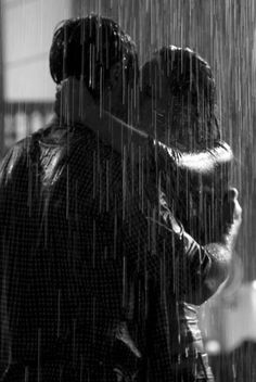 two people standing under an umbrella in the rain, one is hugging the other's head