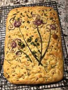 a square pastry with onions and herbs on it sitting on a cooling rack next to a marble counter top