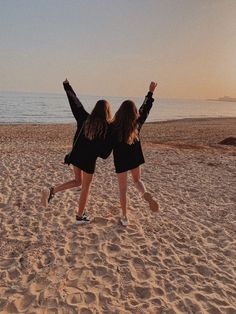 two women are standing on the beach with their arms in the air