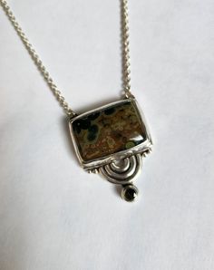 One of a kind sterling silver asymmetric geometric semicircle statement pendant.  Bezel set with a rectangular brown and green colored hasper cabochon and a faceted 4mm green tourmaline. A 16 inch chain is attached. Designed and handcrafted by Richelle Leigh using the lost wax casting process. Free shipping US. https://richellejewelry.etsy.com Artisan Sterling Silver Rectangular Necklace, Modern Green Rectangular Pendant Jewelry, Unique Sterling Silver Rectangular Necklace, Unique Rectangular Sterling Silver Necklace, Modernist Handmade Rectangular Jewelry, Unique Rectangular Sterling Silver Jewelry, Modern Brown Gemstone Jewelry, Contemporary Rectangular Jewelry With Polished Finish, Unique Green Square Pendant Jewelry