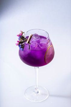 a purple drink in a wine glass with flowers on the rim and a gold stick sticking out of it