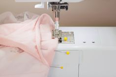 a sewing machine with a pink fabric on it's side and yellow buttons in the background