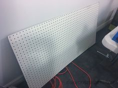 a white pegboard with some red wires attached to it next to a chair and desk