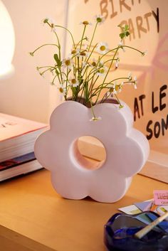 a white flower vase sitting on top of a wooden table next to a book shelf