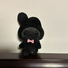 a small black stuffed animal with a pink bow tie on top of a wooden shelf