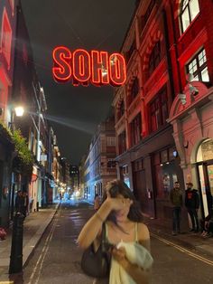 a woman walking down the street in front of a neon sign that says soloo