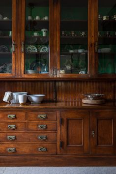 a wooden cabinet with glass doors and dishes on the top shelf in front of it